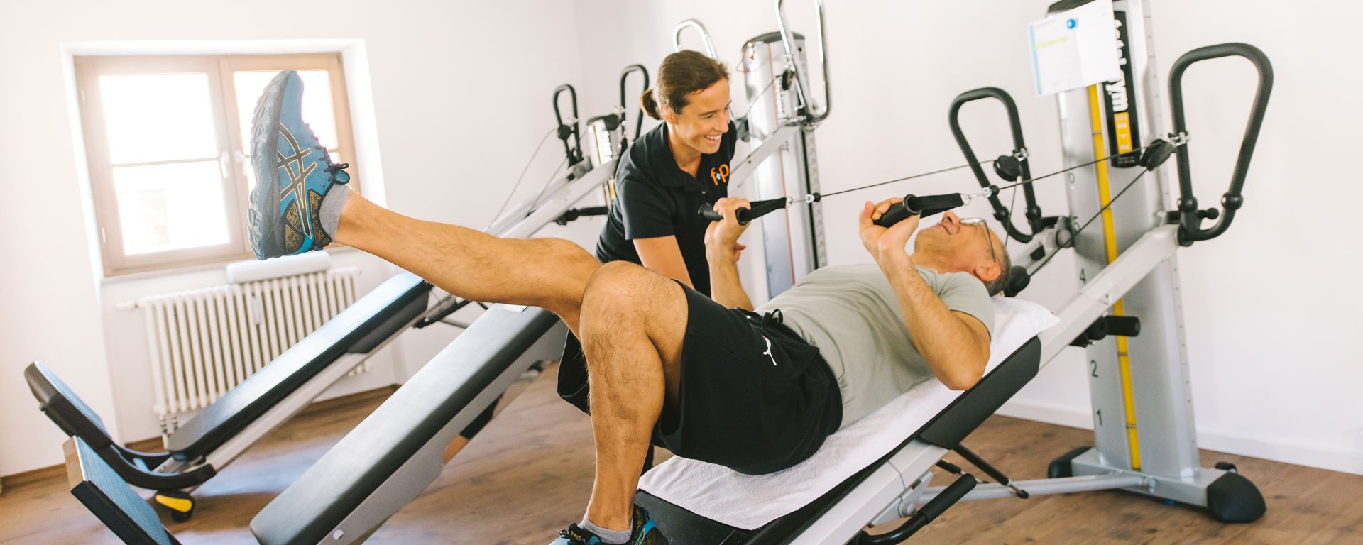 Patient trainiert Beine an einem Gerät mit Trainerin 