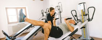 Patient trainiert Beine an einem Gerät mit Trainerin 