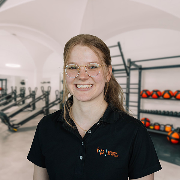 AgWi Kopie Lächelnde Agnes mit Brille und schwarzem f+p-Poloshirt in einem modernen Trainingsbereich der Ergotherapie
