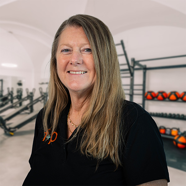 Frau mit langen Haaren in einem Fitnessstudio, lächelnd und in schwarzem Poloshirt.