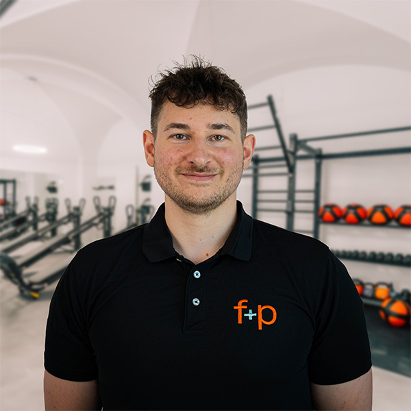 Mann mit kurzen braunen Haaren und Bart, trägt ein schwarzes Poloshirt mit f+p Logo in einem Fitnessstudio.