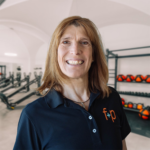 Christine Endres als Physiotherapieexpertin bei f+p Gesund Bewegen im Allgäu, lächelndes Porträt vor Trainingsgeräten in der Praxis.