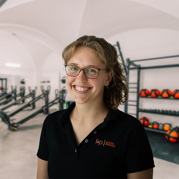 Lächelnde Person mit Brille in einem Fitnessstudio mit Trainingsgeräten im Hintergrund.