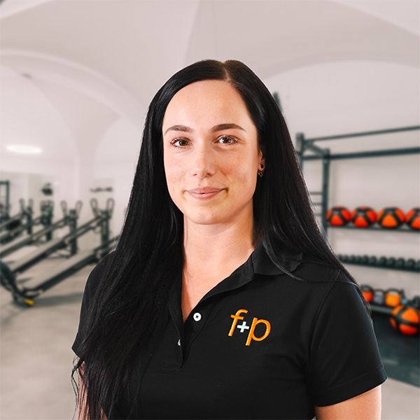 Luise Bernecker Eine Person mit langen, schwarzen Haaren trägt ein schwarzes Polohemd mit einem Logo im Fitnessstudio.