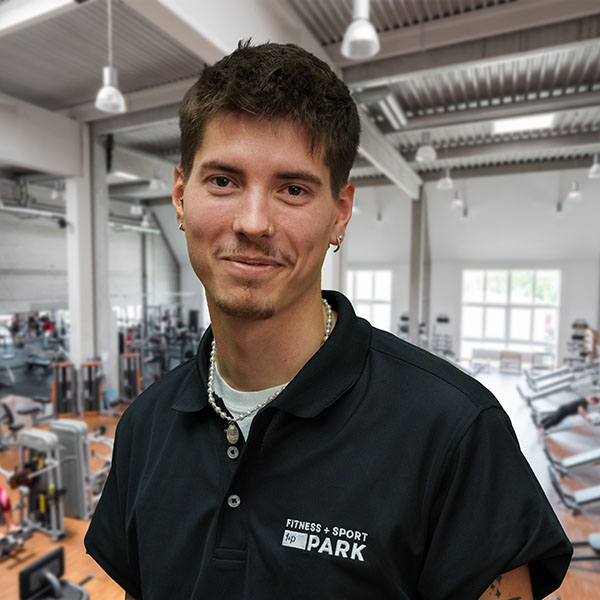Marvin im Fitnessstudio, trägt schwarz polo mit Fitness + Sport Park Logo, lächelt freundlich, helles Studio-Training im Allgäu-Umfeld