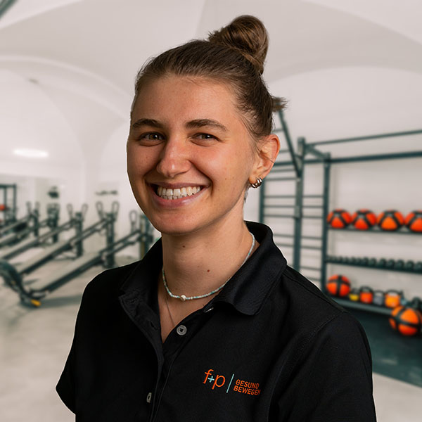 Die Physiotherapeutin Saskia von f+p Gesund Bewegen lächelt in der modernen Trainings- und Rehaumgebung in Kempten im Allgäu vor Hanteln und Geräten.