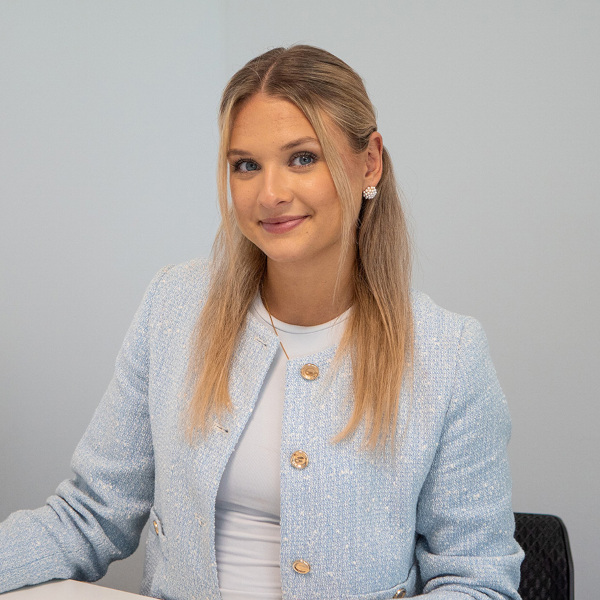 vanenewal Vanessa von f+p Gesund Bewegen in Kempten sitzt am Tisch und blickt freundlich in die Kamera, im hellen Blazer für den Bereich Marketing im Allgäu.