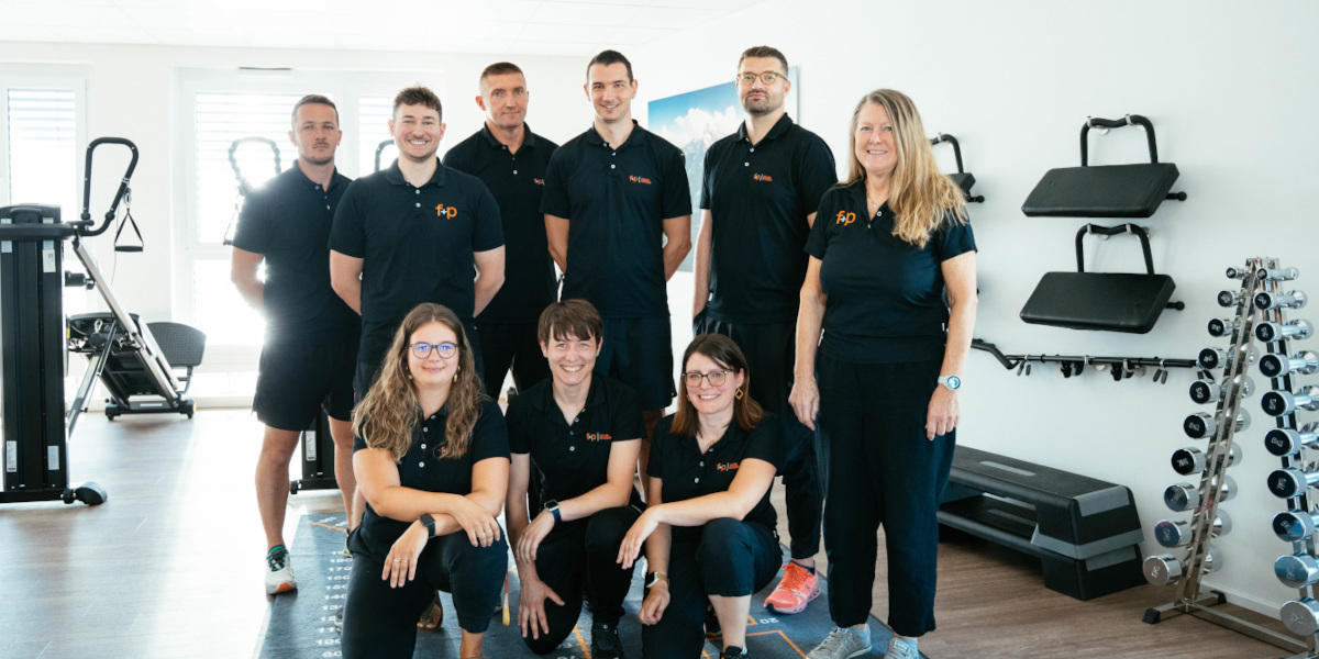 Das f+p-Team in Augsburg-Oberhausen steht gemeinsam in der hellen Praxis für Physiotherapie, Ergotherapie und Reha-Nachsorge bei f+p Gesund Bewegen.