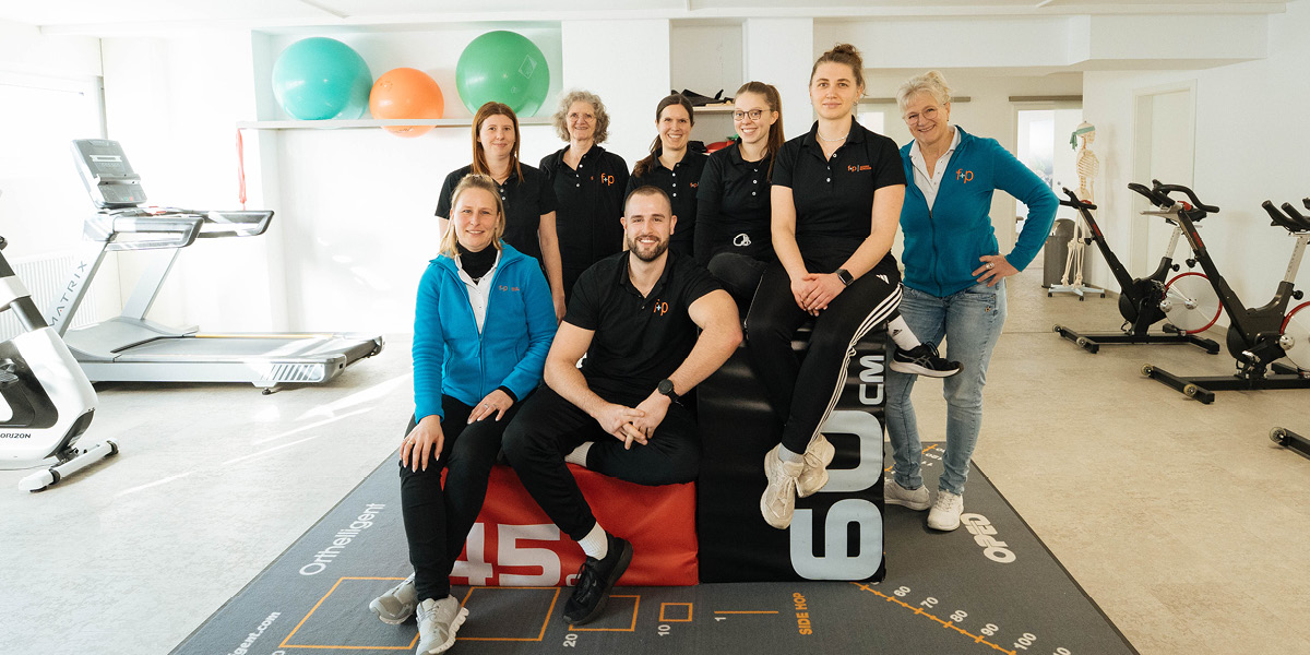 Das Team von f+p Gesund Bewegen posiert in einem Fitnessraum mit Trainingsgeräten und Fitnessbällen.