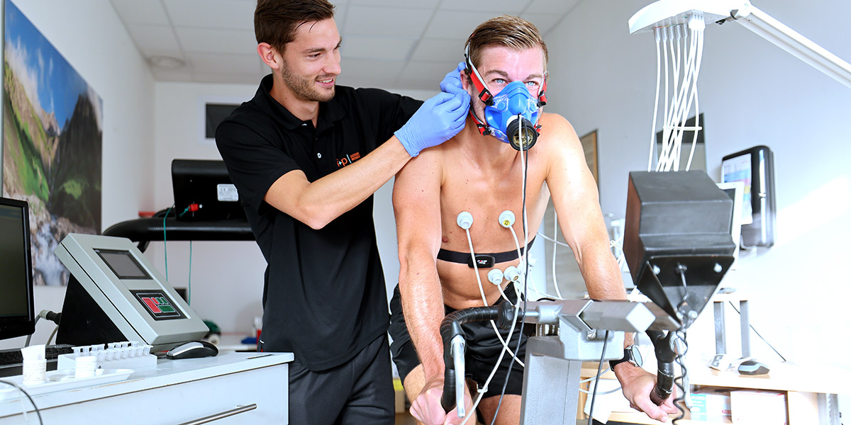 Mann mit Atemmaske und Elektroden während eines sportlichen Leistungstests in einem Labor.