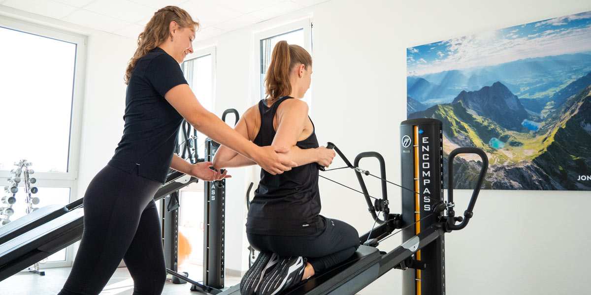 Eine Trainerin unterstützt eine Klientin bei einer Übung auf einem Trainingsgerät in einem Fitnessraum.