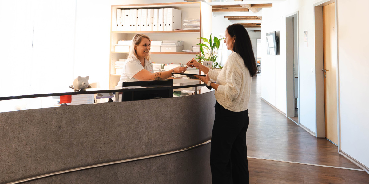 Mitarbeiterin am Empfang übergibt etwas an eine Besucherin in einem modernen Büro.