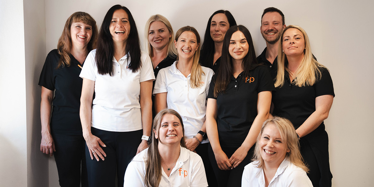 Das Team von f+p Gesund Bewegen, bestehend aus zehn Personen in schwarzen und weißen Poloshirts, lächelt in die Kamera.