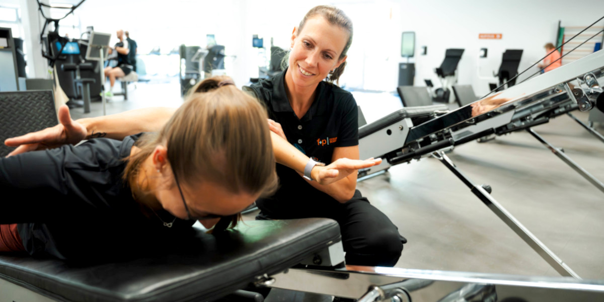 Physiotherapeutin unterstützt eine Patientin bei einer Übung auf einem Trainingsgerät im Fitnessstudio.