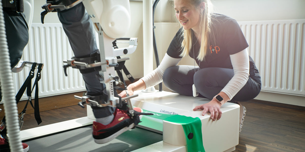 Eine Person nutzt ein Robotik-Hilfsmittel zur Rehabilitation, während eine Fachkraft assistiert.