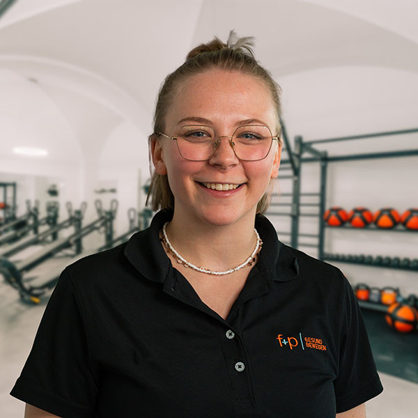 Lächelnde Person mit Brille und schwarzem Poloshirt im Fitnessstudio mit Fitnessgeräten im Hintergrund.
