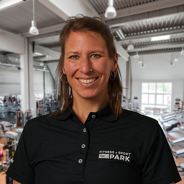 Frau mit kurzen Haaren in einem schwarzen Poloshirt steht in einem Fitnessstudio.