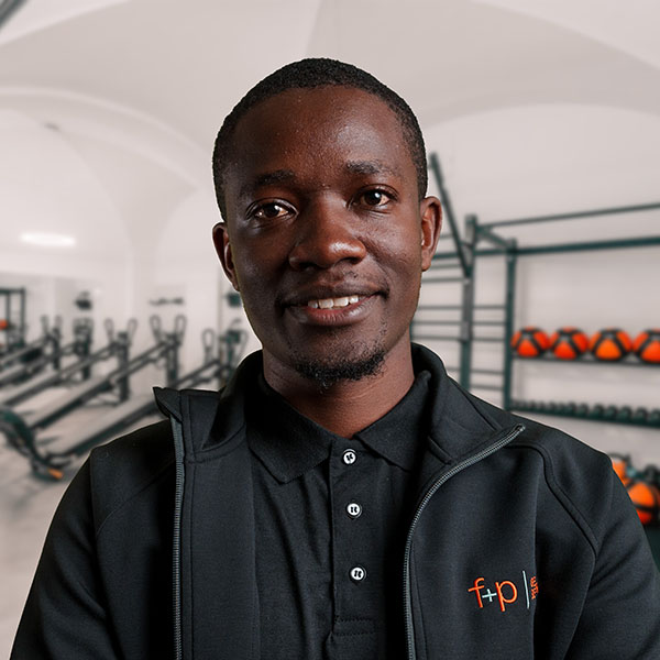 ElijaKi Mann mit dunkler Hautfarbe trägt eine schwarze Jacke mit dem Logo von f+p Gesund Bewegen.