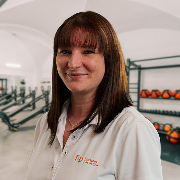 Frau mit braunen Haaren in einem Fitnessstudio, trägt ein weißes Polohemd mit Logo.