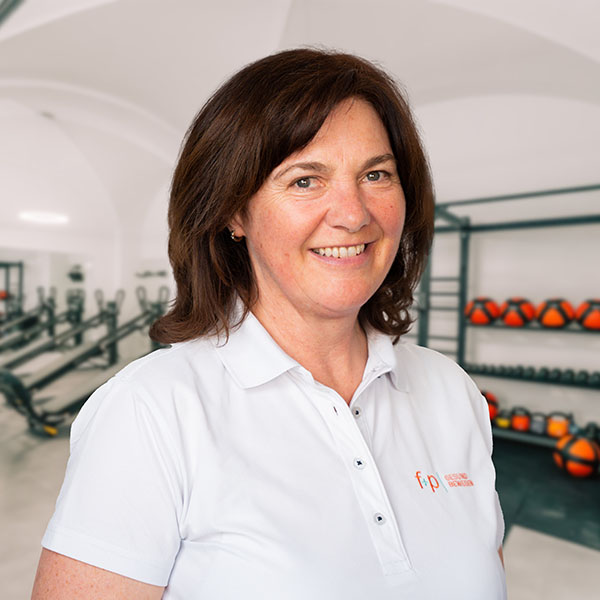 Luise von f+p Gesund Bewegen mit braunen Haaren und weißem Polo in der Trainingspraxis des Allgäus, im Hintergrund Geräte und Hanteln sichtbar