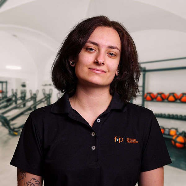Sofie Schmidt Junge Frau mit dunklen Haaren in einem schwarzen Poloshirt vor einer Fitnessumgebung.