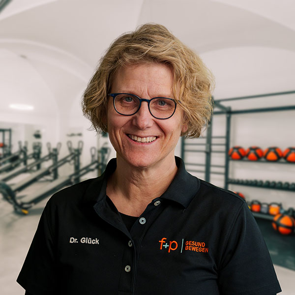 Dr. Glück steht in einem Fitnessstudio mit Trainingsgeräten im Hintergrund.