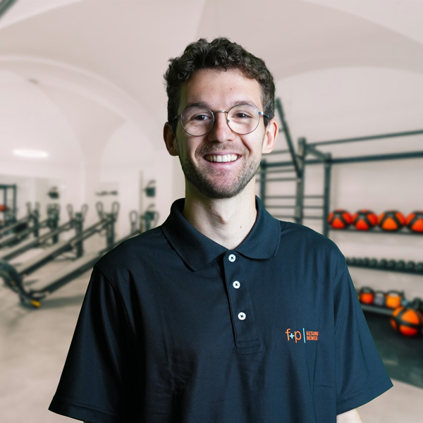 Mann mit Brille trägt ein schwarzes Poloshirt und lächelt in einem Fitnessstudio.