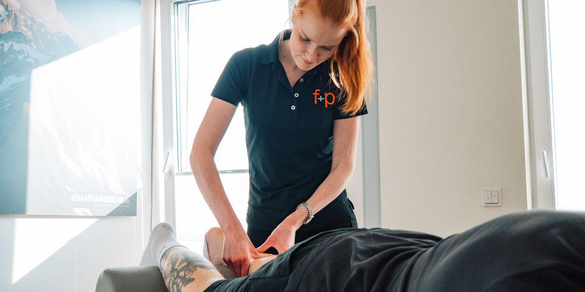 Eine Masseurin führt eine Massage an einem liegenden Klienten in einem hellen Raum durch.