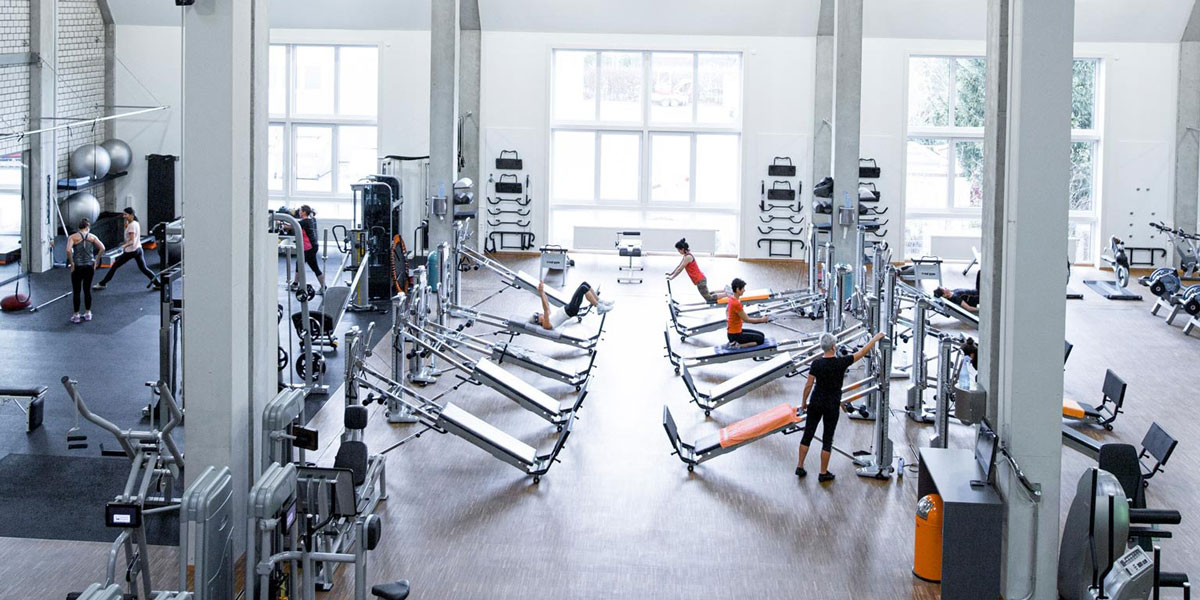 Innenansicht eines Fitnessstudios mit verschiedenen Trainingsgeräten und Personen beim Training.