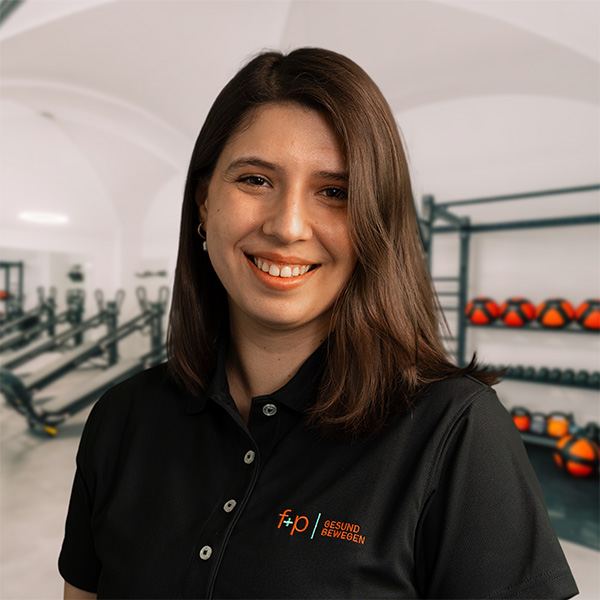 Gizem Yilmaz Frau mit dunklen Haaren in einem schwarzen Poloshirt lächelt vor einer Fitnessstudio-Hintergrund.