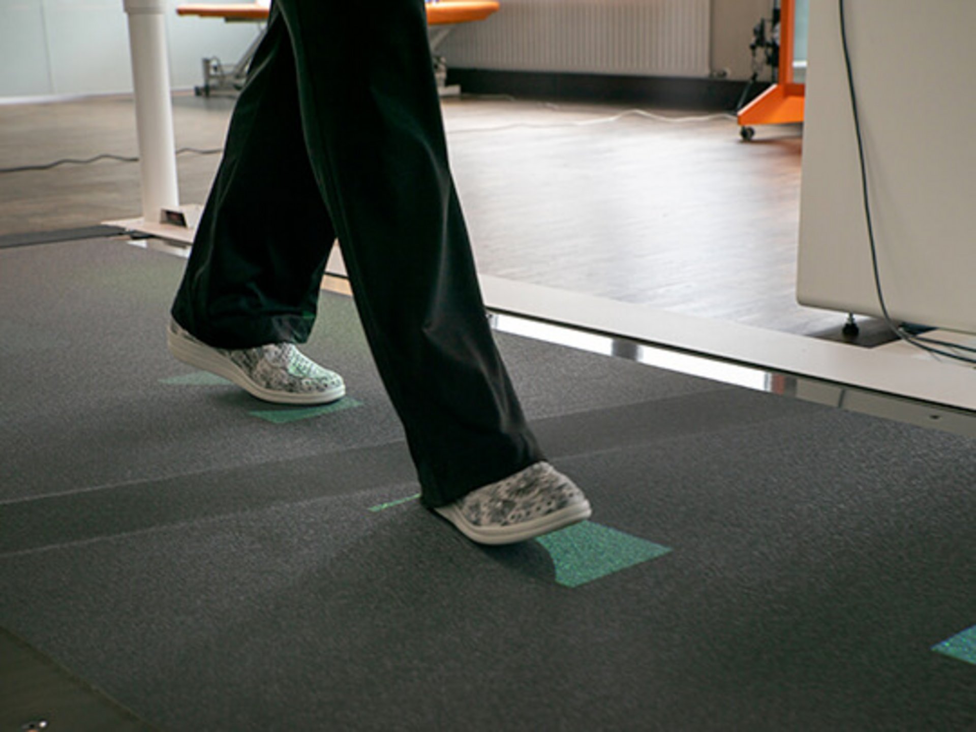 csm_c_millschrittlaenge_8a0f5e3241 Eine Person mit grauen Schuhen geht auf einem Laufband mit grünen Markierungen.