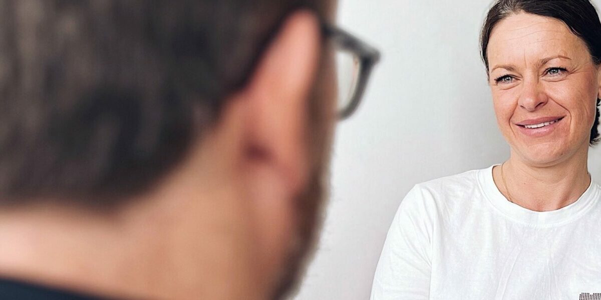 Eine Frau mit lächelndem Gesicht, die einem Mann im Gespräch gegenüber sitzt.