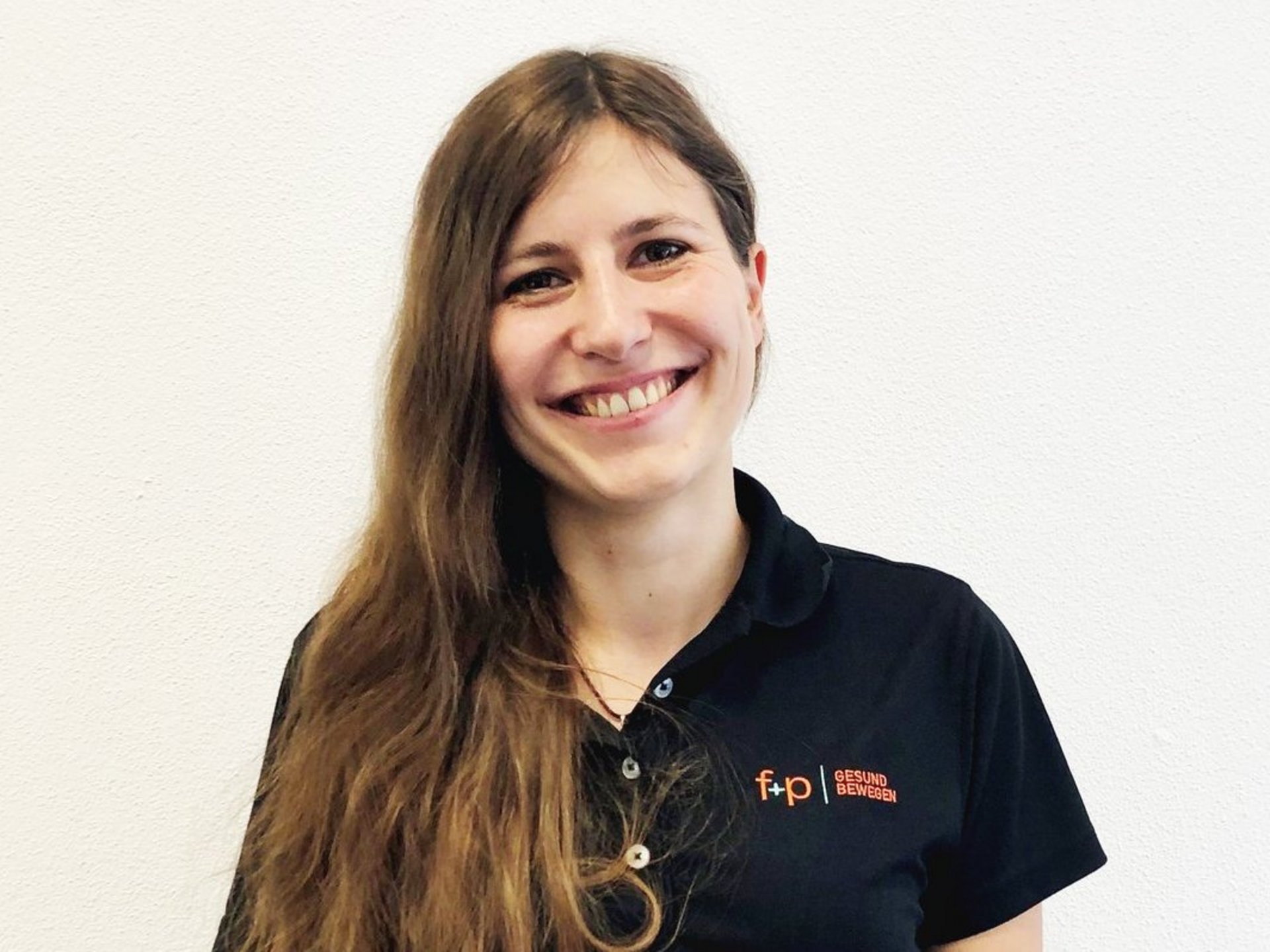 csm_f_p_personal_Regina-Lupper_94d24498e6 Frau mit langen, braunen Haaren und einem schwarzen Poloshirt mit Logo von f+p gesund bewegen.