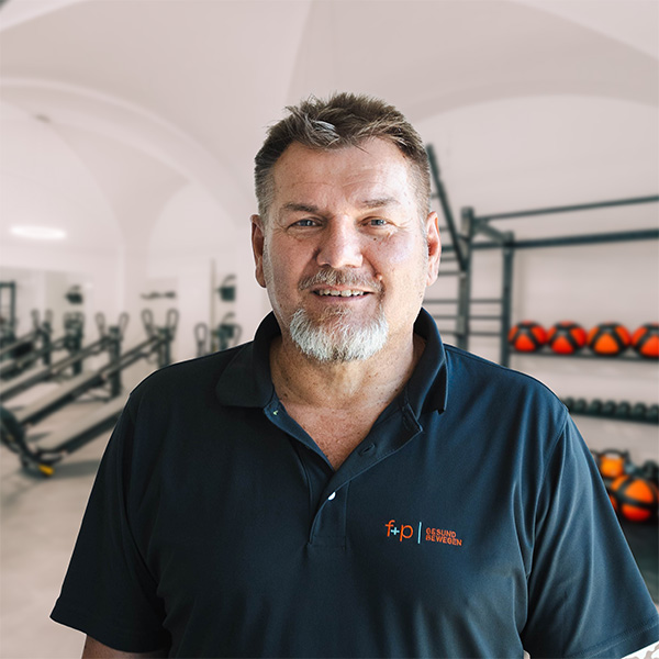 Mann mit Bart trägt ein schwarzes Polo-Shirt mit Logo in einem Fitnessstudio.