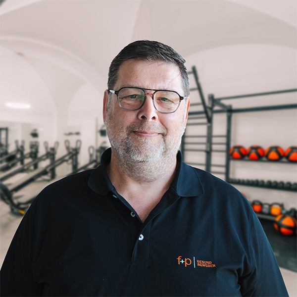 Porträt eines Mannes mit Brille und schwarzem Polo-Shirt im Fitnessstudio.