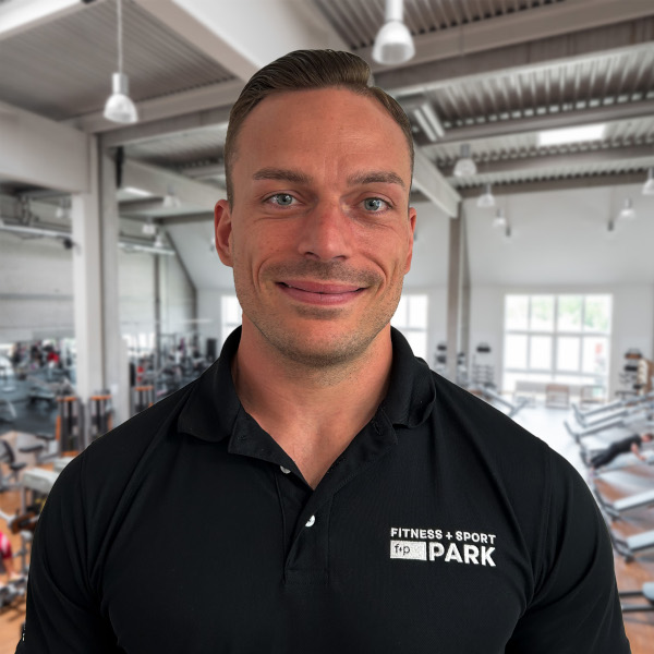 Mann mit kurzem Haar und freundlichem Lächeln, trägt ein schwarzes Polohemd mit dem Logo von Fitness + Sport.
