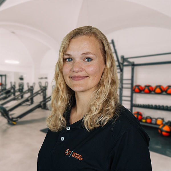 In der Ergotherapie bei f+p Gesund Bewegen in Kempten steht Lena vor modernen Trainingsgeräten, Medizinbällen und dem Therapieraum im Allgäu.