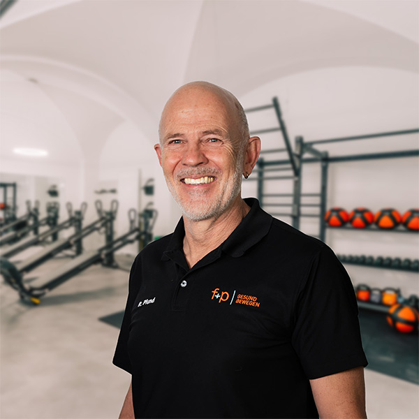 Mann mit Glatze und Bart in schwarzer Sportkleidung lächelt in einem Fitnessstudio.