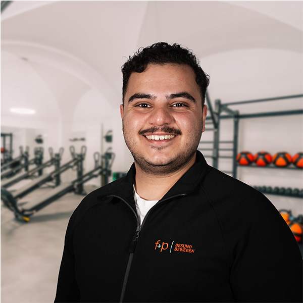 Lächelnder Mann in schwarzer Sportjacke mit Logo vor einer Fitnessumgebung.