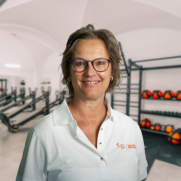Eine Person mit Brille und einem weißen Poloshirt steht in einem Fitnessstudio mit Fitnessgeräten im Hintergrund.