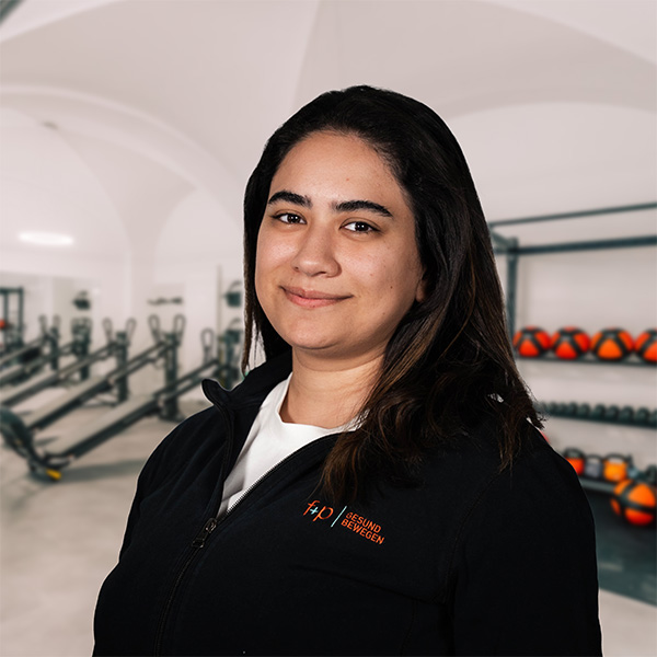 Eine Person in Sportbekleidung mit einem Lächeln steht vor Fitnessgeräten in einem Trainingsraum.