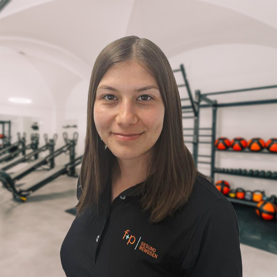 Stefana, Physiotherapeutin bei f+p Gesund Bewegen, trägt ein schwarzes Teamshirt und lächelt in der Trainingshalle mit roten Hanteln in Kempten.