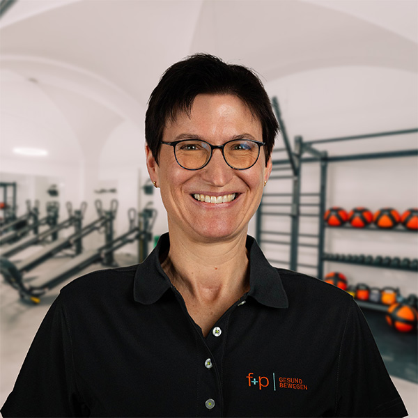 MarionSo Frau mit kurzen, dunklen Haaren und Brille, trägt ein schwarzes Poloshirt mit Logo von f+p Gesund Bewegen.