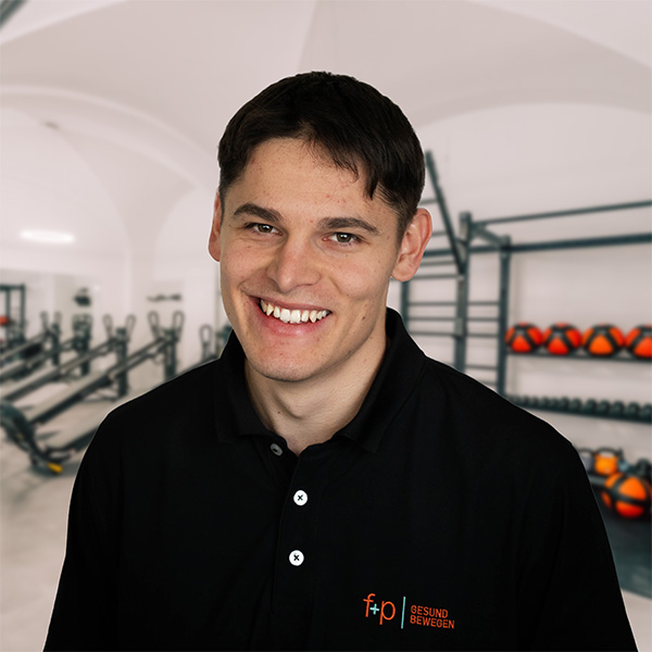SimonSo Mann mit kurzem Haar und freundlichem Lächeln, trägt ein schwarzes Poloshirt mit Logo von f+p Gesund Bewegen.