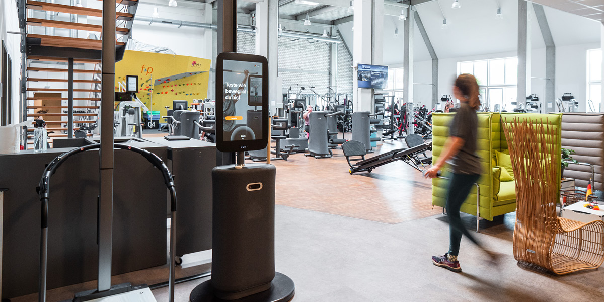 Moderne Fitnessstudio-Ausstattung mit Trainingsgeräten und einem interaktiven Bildschirm im Vordergrund.