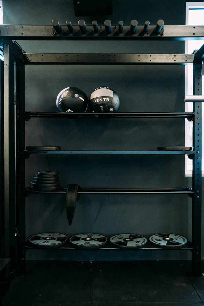 Schwarze Trainingsgeräte mit Medizinbällen und Gewichtsscheiben auf Regalen in einem Fitnessstudio.