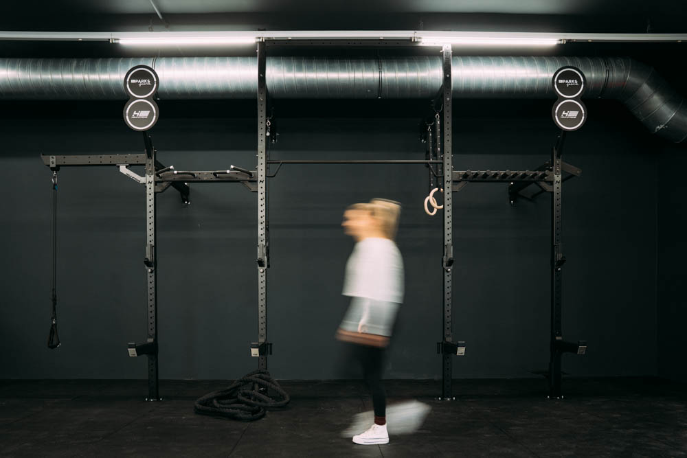 Frau in Bewegung vor einer schwarzen Trainingsstation mit Fitnessgeräten in einem modernen Fitnessstudio.