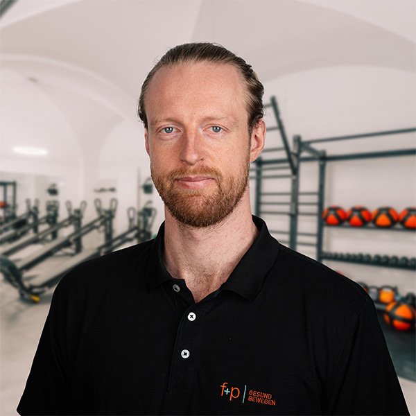 JaHa Mann mit Bart in schwarzem Poloshirt vor einer Fitnessumgebung mit Geräten und Gewichten.