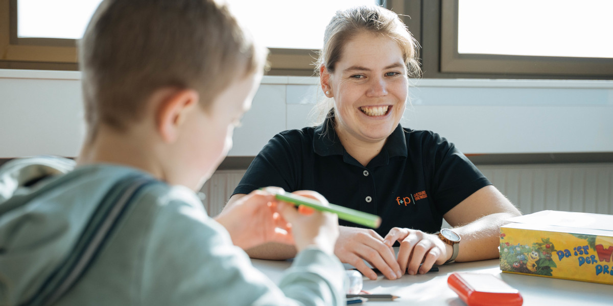 Eine Ergotherapeutin lächelt während einer Sitzung mit einem Kind, das mit einem Stift an einem Tisch arbeitet.
