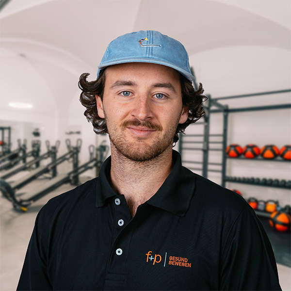 Mann mit blauer Kappe und schwarzem Polohemd von f+p Gesund Bewegen in einem Fitnessstudio.